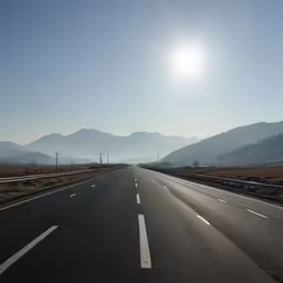an empty highway with the sun beaming down on the mountains