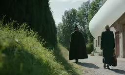 a couple of people walking on a dirt road next to some bushes