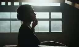 a woman holding her hand to her temple looking out the window