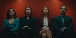 three women and a man are sitting in front of red walls