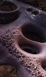 a tire with holes sitting next to some dirt