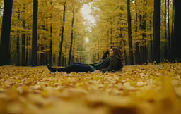 a beautiful young woman laying on the ground in an autumn leaf covered forest