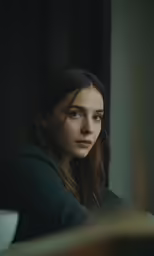 a woman in a dark room looking out the window