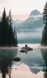 a person sitting on a rock in the water near mountains