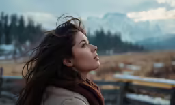 woman with her hair blowing in the wind near a fence