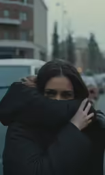 woman holding arm around the neck of another person while standing near some cars