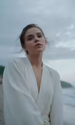 woman in white robe standing on beach near water