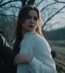 a beautiful young woman wearing a white jacket and standing by a forest