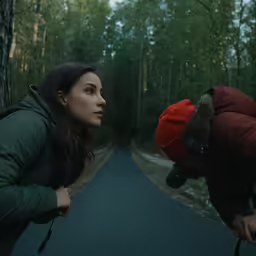 a person in a jacket and a red hat looks off at another person