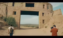 two men walking down the dirt road through the rock structure