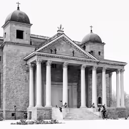 black and white photograph of people riding bicycles in front of an old building
