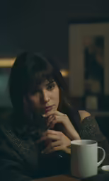 a woman at a table leaning on her hand near a coffee mug