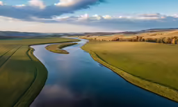 a river surrounded by lush green hills under a cloudy blue sky