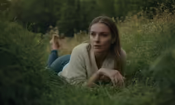 a young girl laying on the ground in a field
