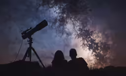 two people are sitting next to a telescope