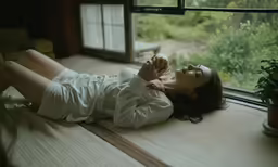 a woman is lying on the windowsill next to a plant