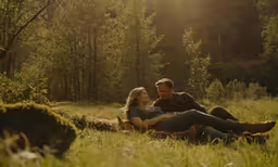 man and woman sitting on tree stump in the woods