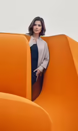 a young woman standing behind a structure made from orange pieces