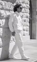 a person leaning against a stone wall wearing white pants