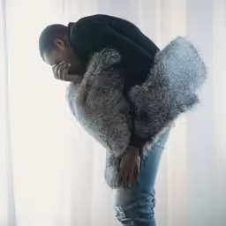 a black man is looking down wearing a furry coat