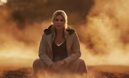 a young woman sitting on a sandy ground next to fog