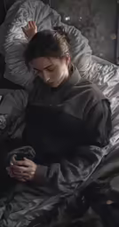 a woman sits on her bed looking at her phone