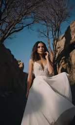 a beautiful woman in a long white dress walking on a rock formation