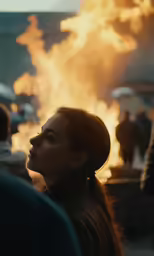 a woman in a head scarf looking away at a large fire