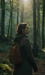 a woman wearing a backpack looking up in the forest