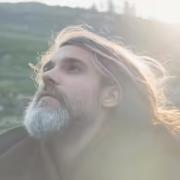 man with grey beard and long hair looking upwards