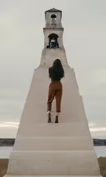 the little girl in brown is looking at the bell tower