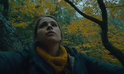 a woman standing near some trees, and looking up