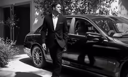 a man in a tuxedo stands next to a car
