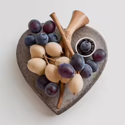 a heart - shaped slate cheese dish that features olives, grapes, and a saucer
