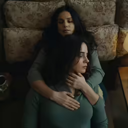 two women hugging one another while standing in front of a couch