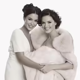 two women dressed in evening dresses pose for a photo