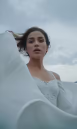 a woman in white dress and a blanket blowing in the wind