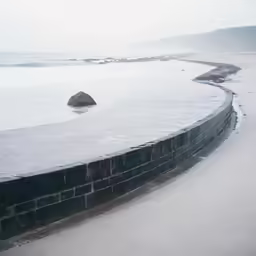 a wet walkway with sand and water near the ocean