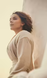a woman in beige clothing leaning on a wall
