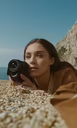a woman in a yellow shirt is taking a photo on a rocky beach