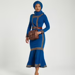 a woman in a blue dress and head scarf poses for the camera