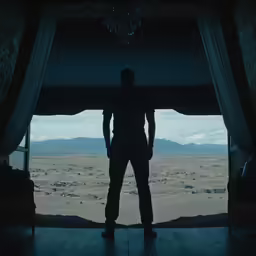 man standing in open doorway of desert overlooking valley
