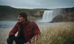 man in brown hat sitting near water falls