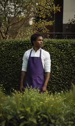 a black man in aprons standing near a hedge