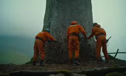 three people in orange uniform on mountain with tree