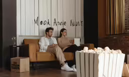 a couple sitting on a couch with a movie popcorn in front of them