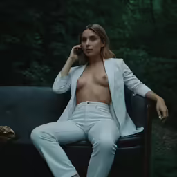 a shirtless woman is sitting on a chair talking on a cellphone