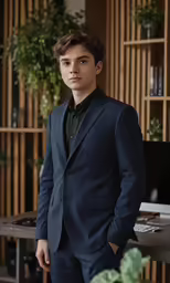 a boy in a suit standing next to a table and bookshelves