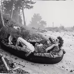 a woman lying in a small canoe on the beach