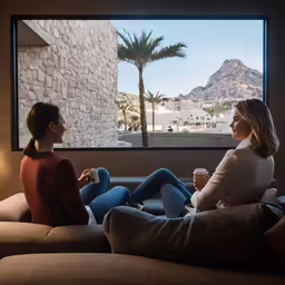 two women looking out a window while sitting on couches